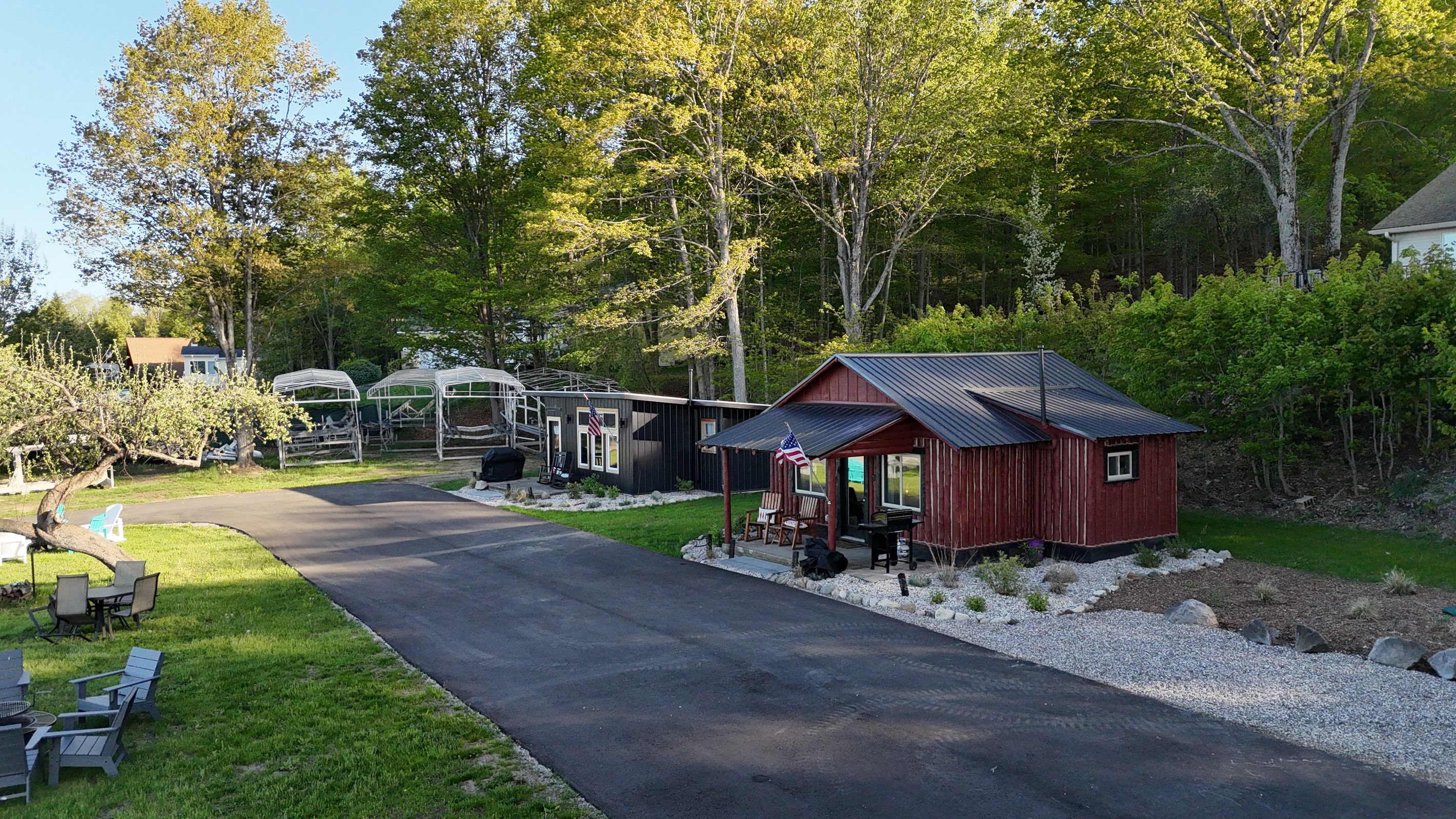 A rustic cabin with a metal roof, surrounded by a gravel path and greenery.