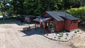 A rustic cabin with a porch, a covered outdoor seating area, and an American flag. - Vintage Lakefront Cabin-Fire Pit-Grill-Lake Views (BOYNE CITY)