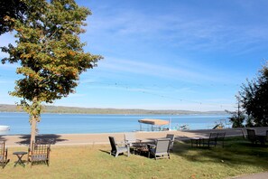 Un espace extérieur aménagé au bord du lac, avec des tables et des chaises, une table de pique-nique couverte et une vue sur le lac.