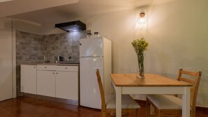 A compact kitchen with a refrigerator, a stove, and a sink. There is a dining table with chairs and a vase with flowers. - The Green Attic by Wonderful Italy (Torino)