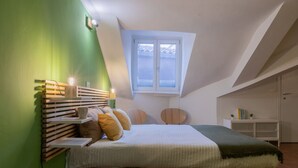 A bedroom with a sloped ceiling, a bed with a wooden headboard, a window, and a small white cabinet. - The Green Attic by Wonderful Italy (Torino)