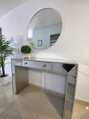 A mirrored vanity with a round mirror, a small potted plant, and a framed picture on the wall. - Ashford Avenue Beach Front Condo (San Juan)