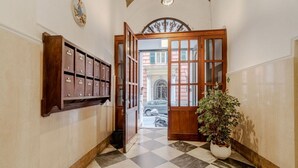 Un couloir avec un sol à carreaux, des meubles en bois, une plante en pot et une porte donnant sur un espace extérieur.
