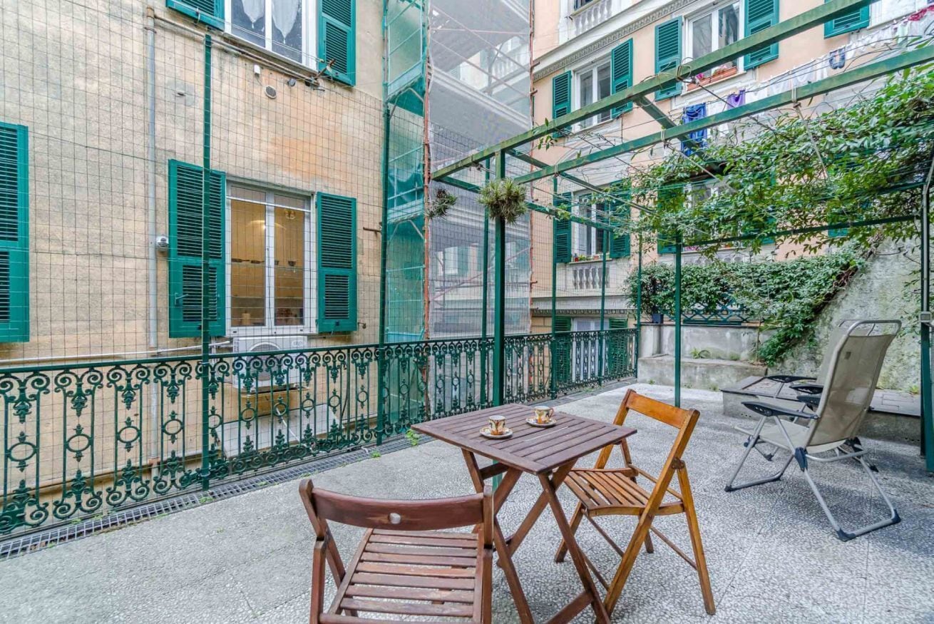 A balcony with a table and chairs, a metal railing, and a building with green shutters.