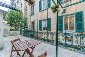 A courtyard with a wooden table and chairs, a metal fence, and buildings with green shutters. - GuestHost - Spacious and welcoming 120 square meters apartment, perfect for six people, located on the second floor of a historic building with an elevator (NOT accessible to disabled guests).The property is centrally located in Genoa, just a 5-minute wa (Genoa)