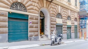 Un bâtiment à la façade en pierre, une entrée avec des volets verts et un scooter garé devant.