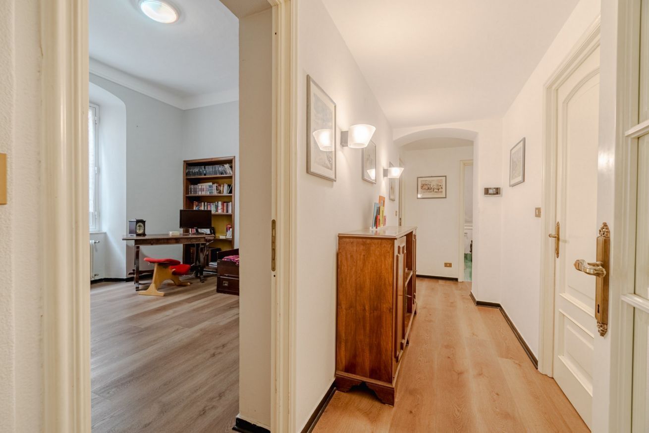 Um corredor com piso de madeira, uma estante e uma porta com puxador de latão.