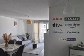 Un salon moderne avec un canapé, une table à manger et un mur où sont affichés différents logos de services de diffusion en continu.