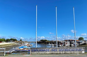 A marina with boats docked, a sign reading 'ESPLANADE DES OSTREICULTEURS,' and a clear blue sky. - Self-contained studio near Port de Larros (Gujan-Mestras)