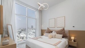 Ein Hotelzimmer mit großem Fenster, einem Bett mit Kissen, einem Nachttisch mit Lampe und zwei gerahmten Bildern an der Wand.