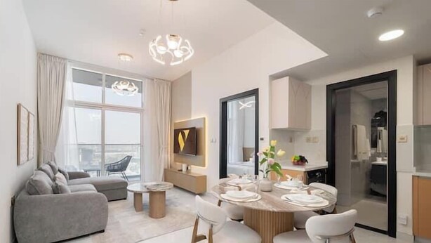 Ein modernes Wohnzimmer mit Sofa, Esstisch, Stühlen, Fernseher und einem großen Fenster.