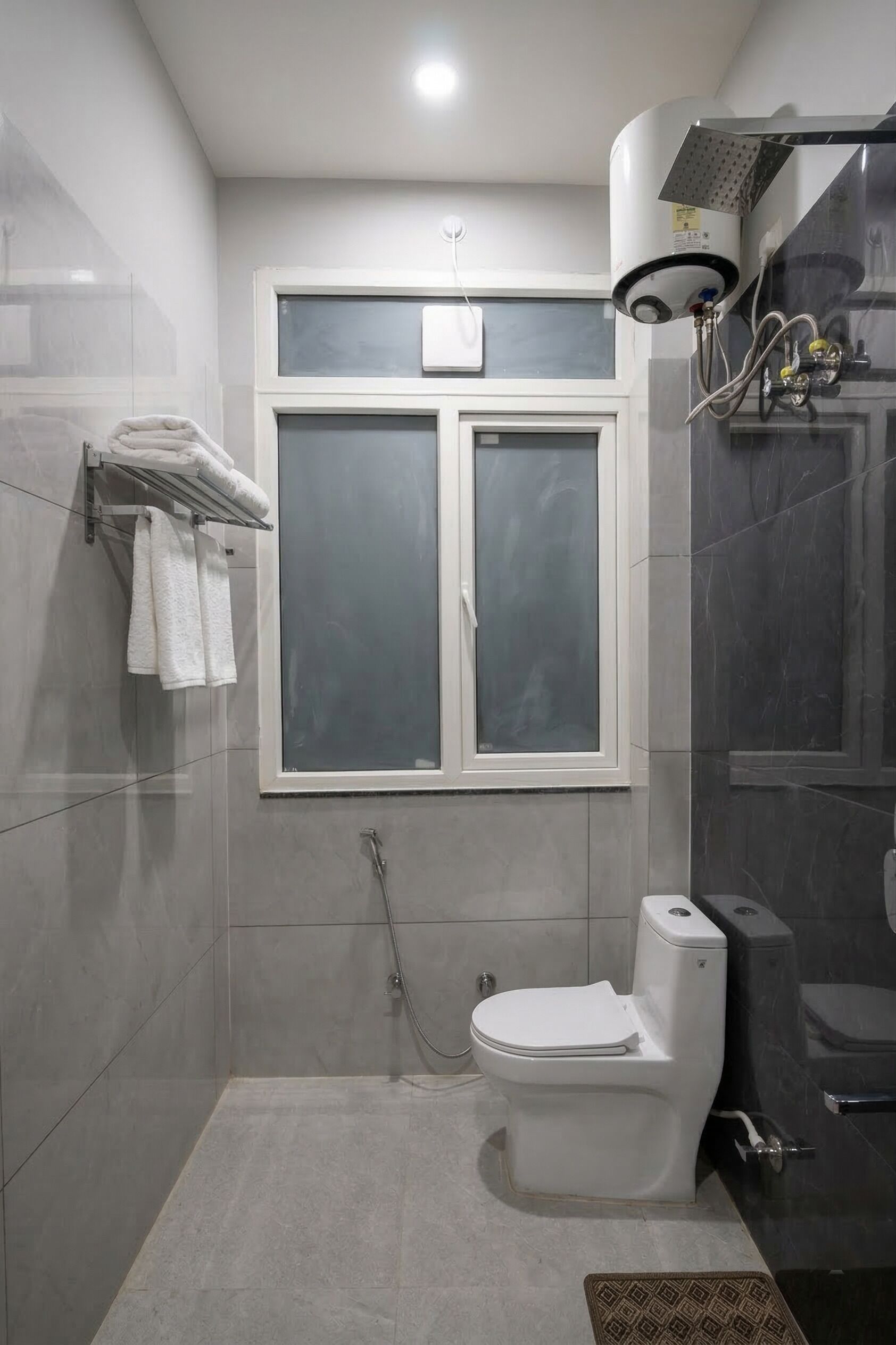 A bathroom with a toilet, a window, a towel rack, and a shower area.