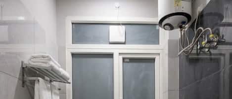 A bathroom with a toilet, a window, a towel rack, and a shower area.