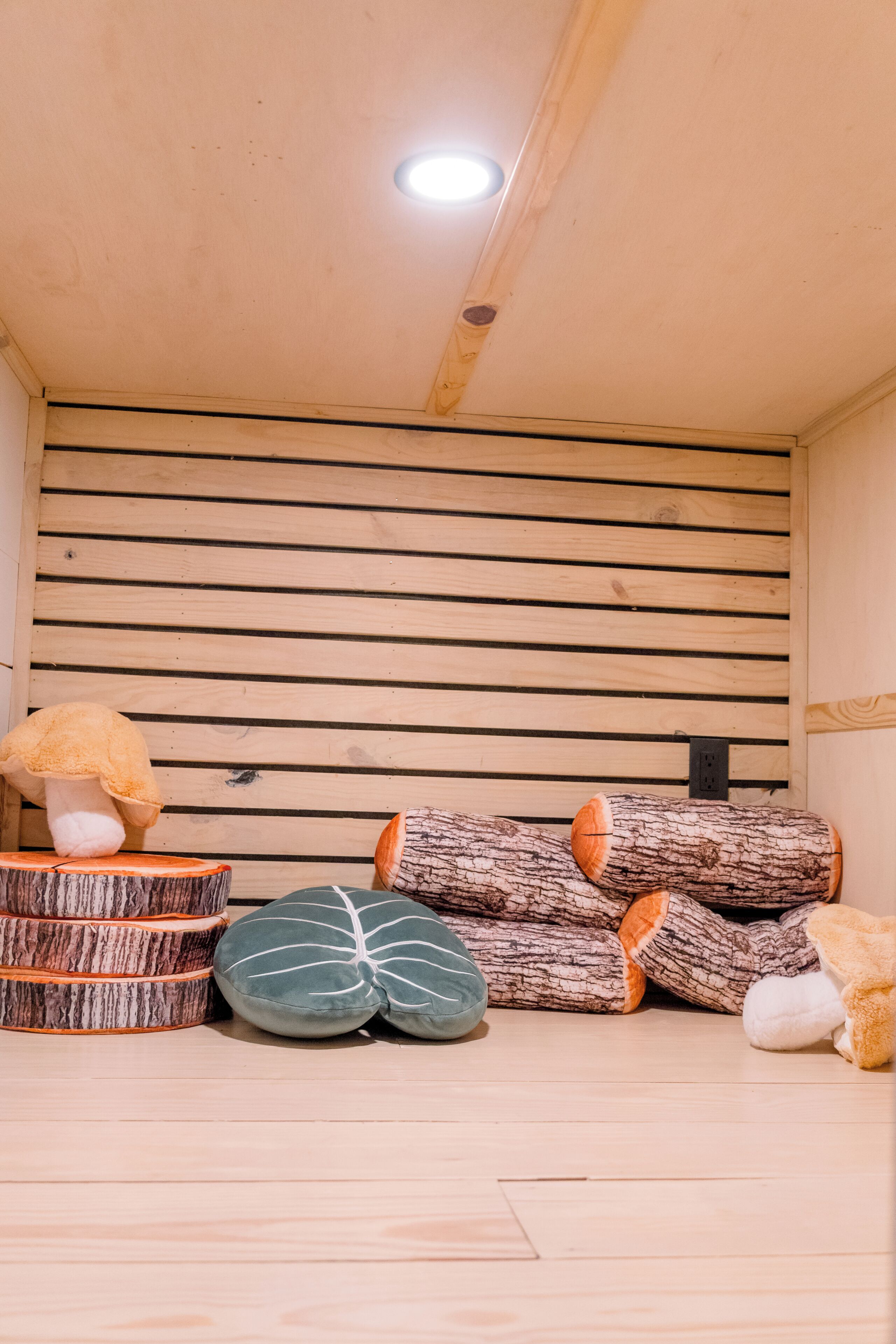 Una stanza con listelli di legno sulla parete, una luce a soffitto e una pila di legna.