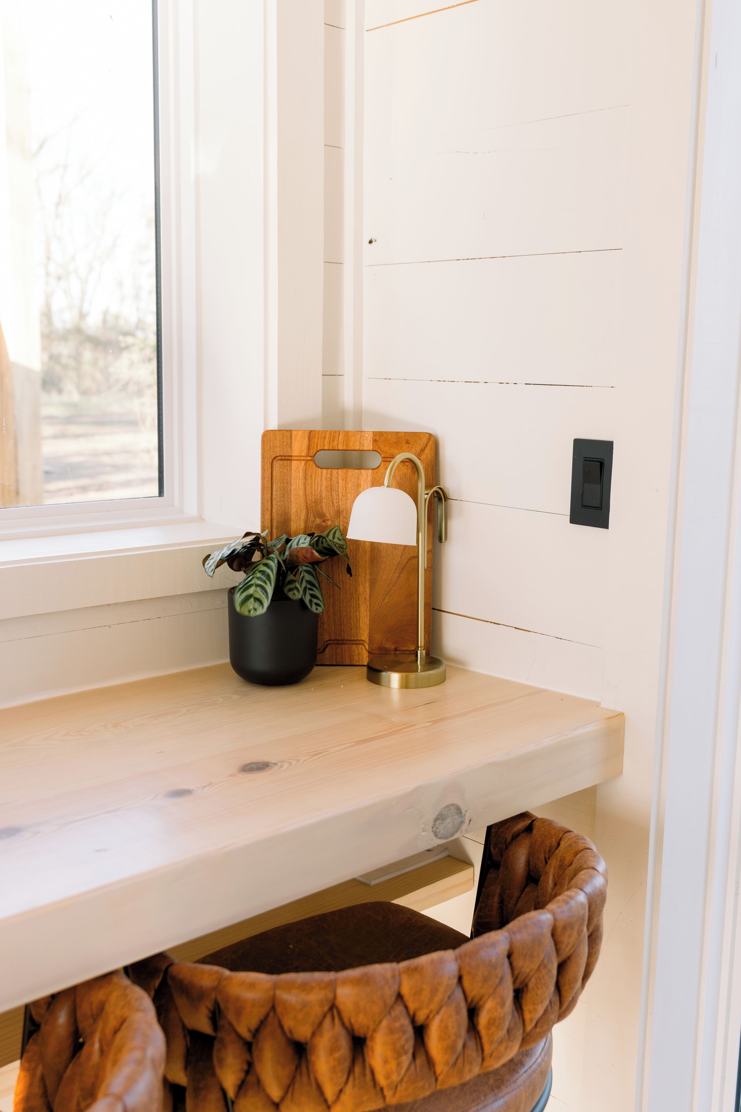 A wooden desk with a potted plant, a lamp, and a chair with a braided design.