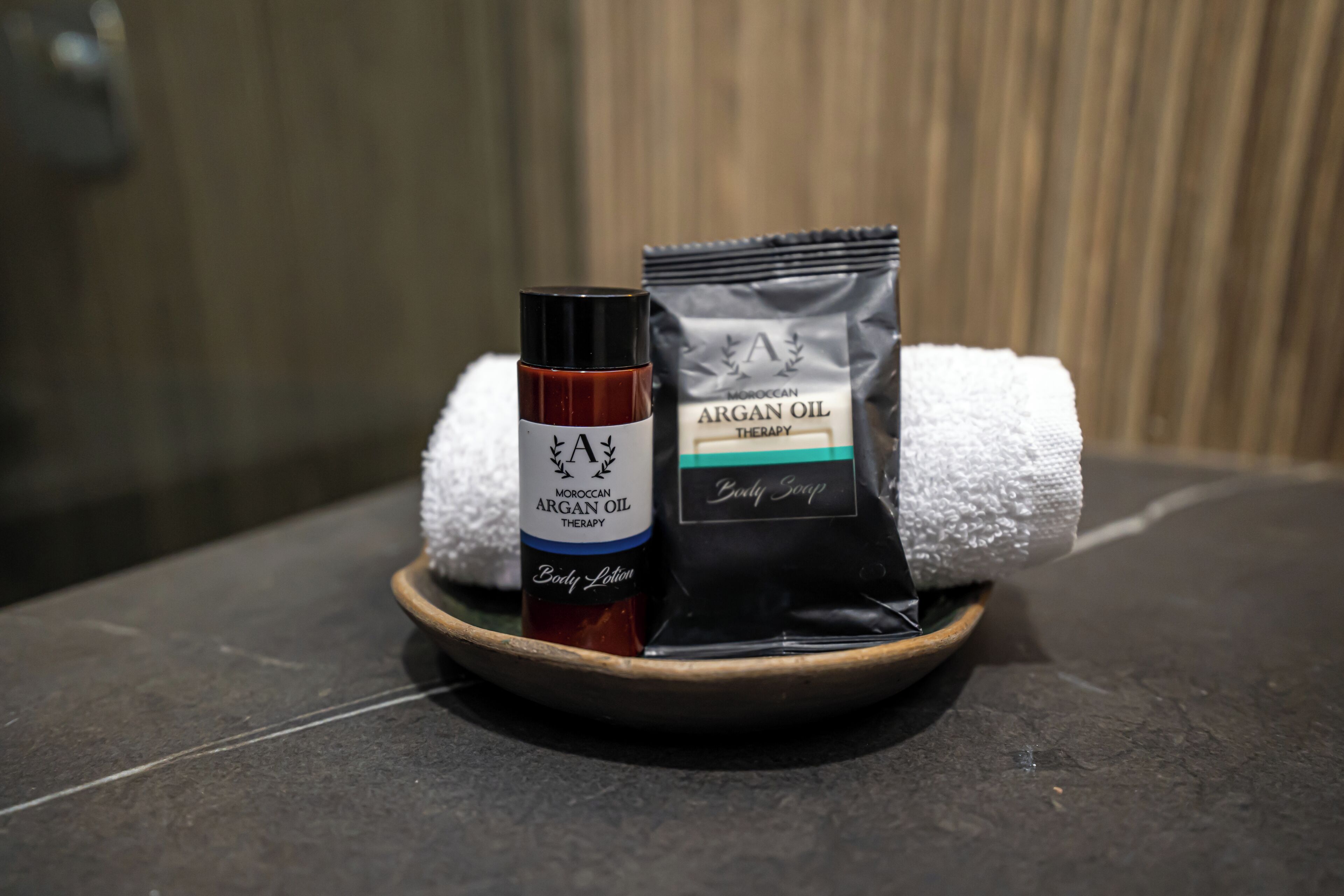 A bottle of Moroccan Argan Oil Therapy, a body lotion, and a packet of body soap on a tray.
