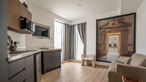 Een moderne keuken met inbouwapparatuur, een eethoek met een bank en een stoel, en een groot raam met gordijnen.
