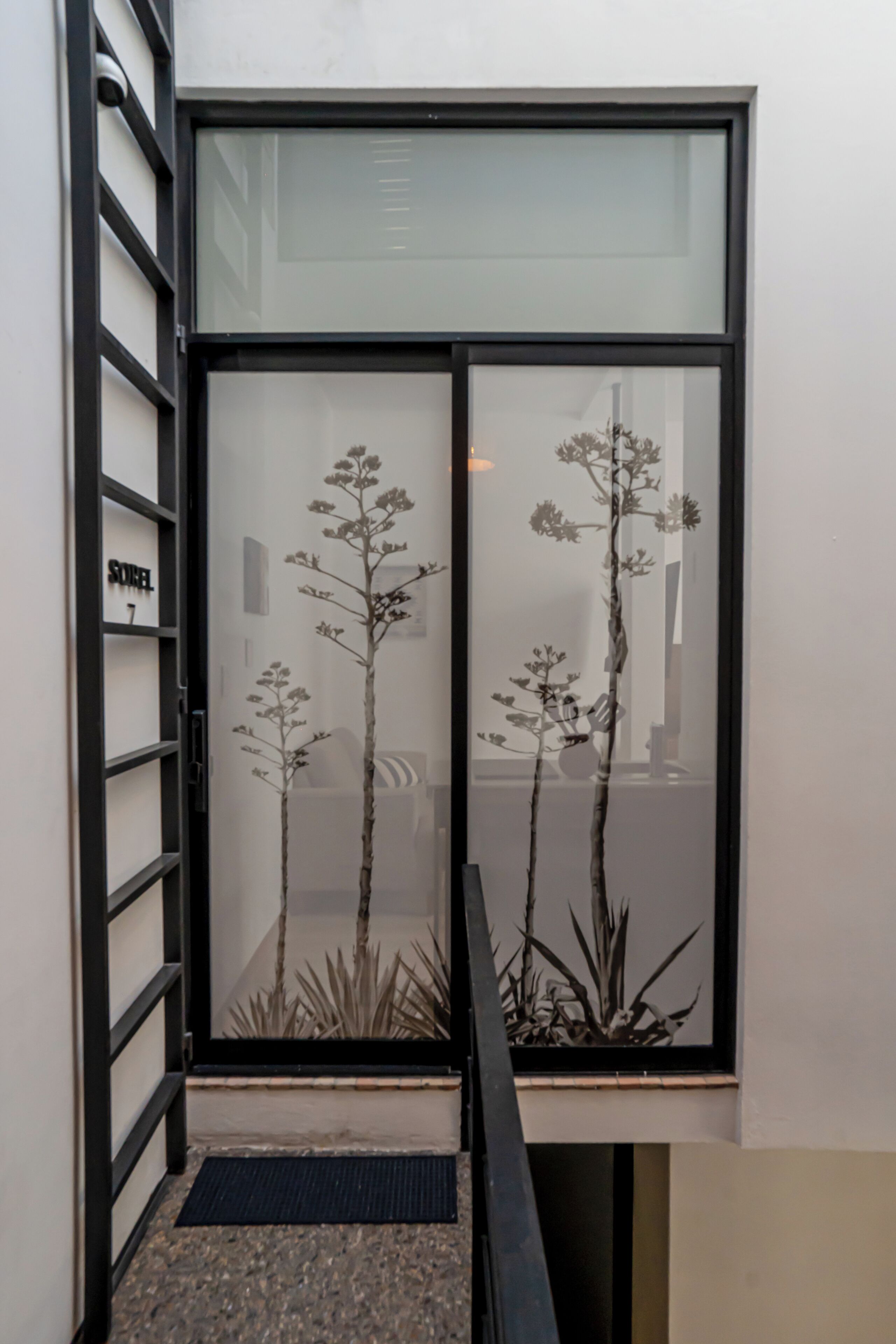 Una entrada de hotel moderna con puerta de cristal, escalera de metal y plantas de interior.