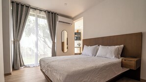 Een slaapkamer met een groot bed, een houten hoofdbord, nachtkastjes, een spiegel en uitzicht op de omgeving door dunne gordijnen.