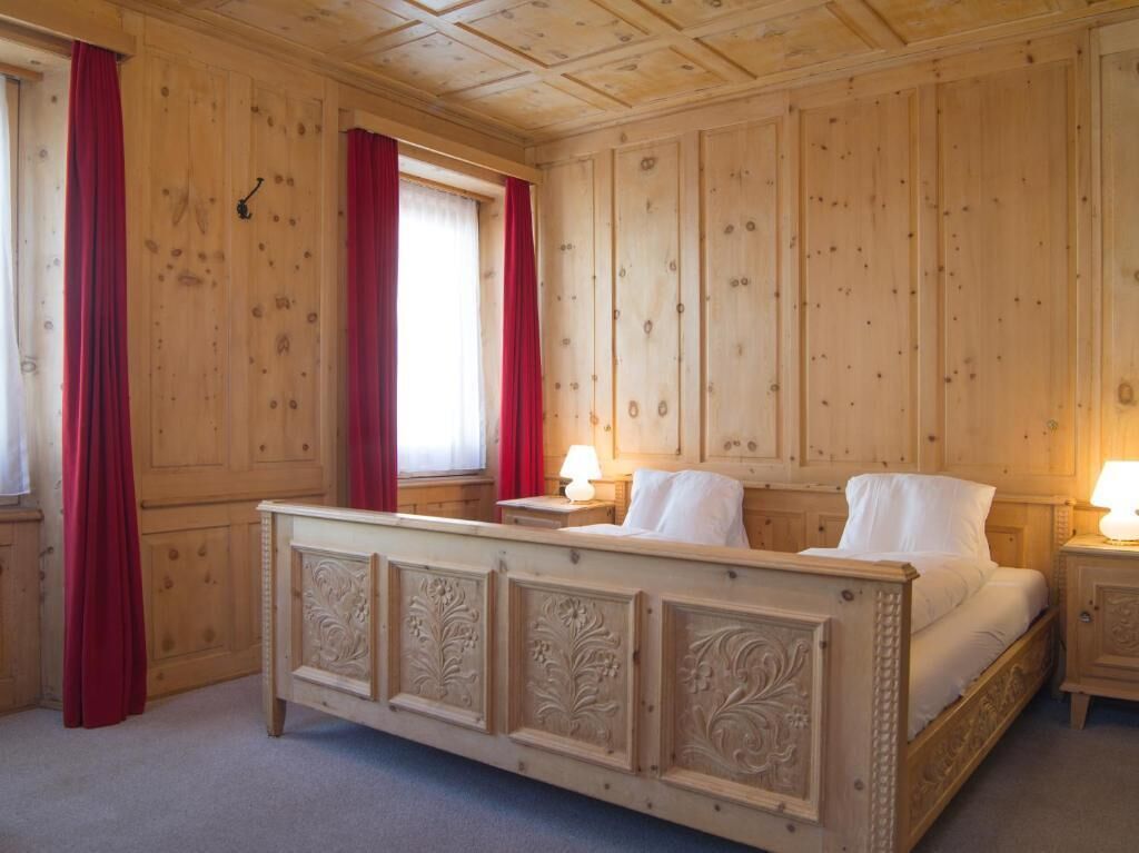 A wooden-paneled room with a bed, two bedside tables, and a window with red curtains.