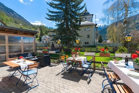 An outdoor patio with tables and chairs, a mountain backdrop, and a building with a tower.