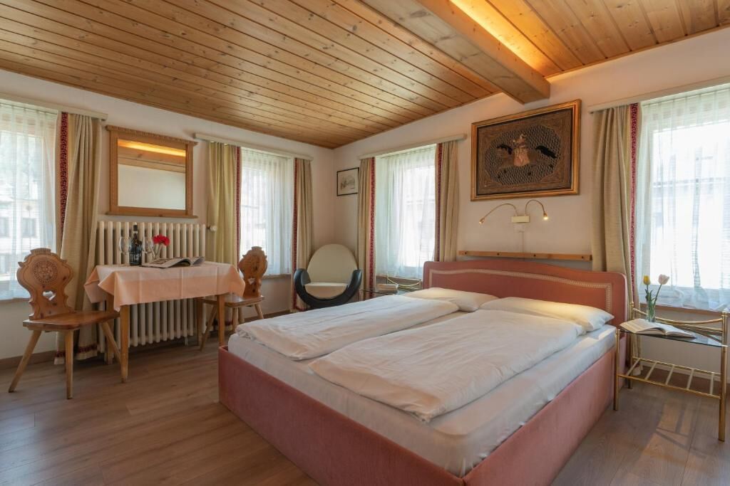 Ett sovrum med en dubbelsäng, ett träpanelat tak, ett element, ett bord med en stol och ett fönster med gardiner.
