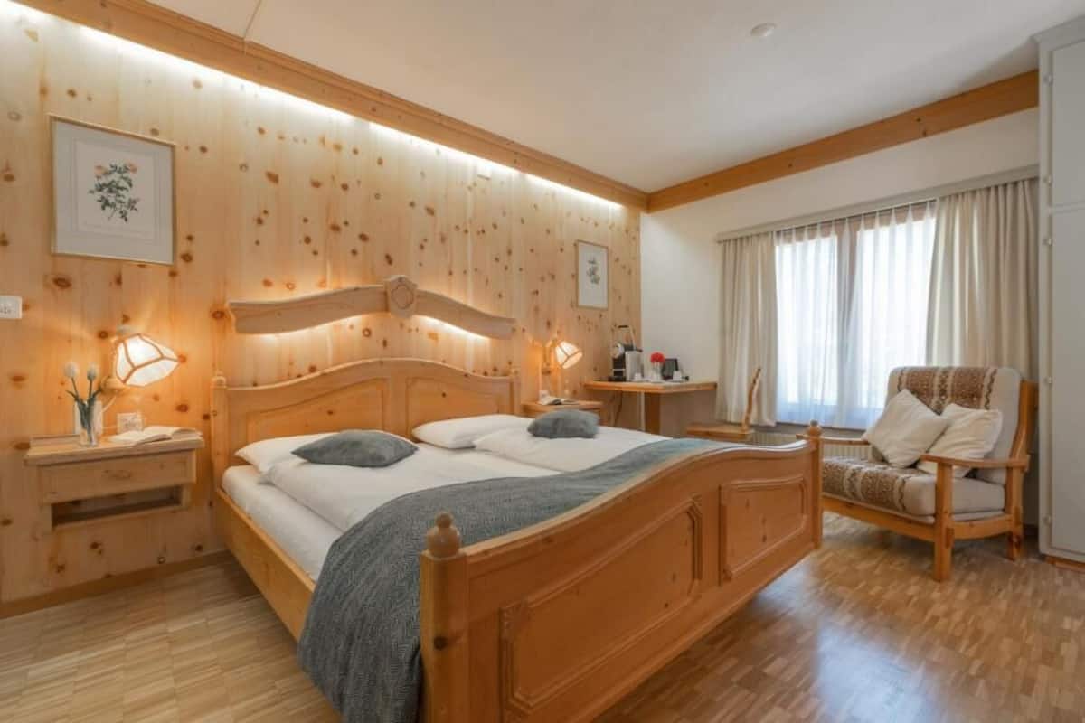 A wooden-paneled bedroom with a bed, bedside tables, a chair, and a window with curtains.
