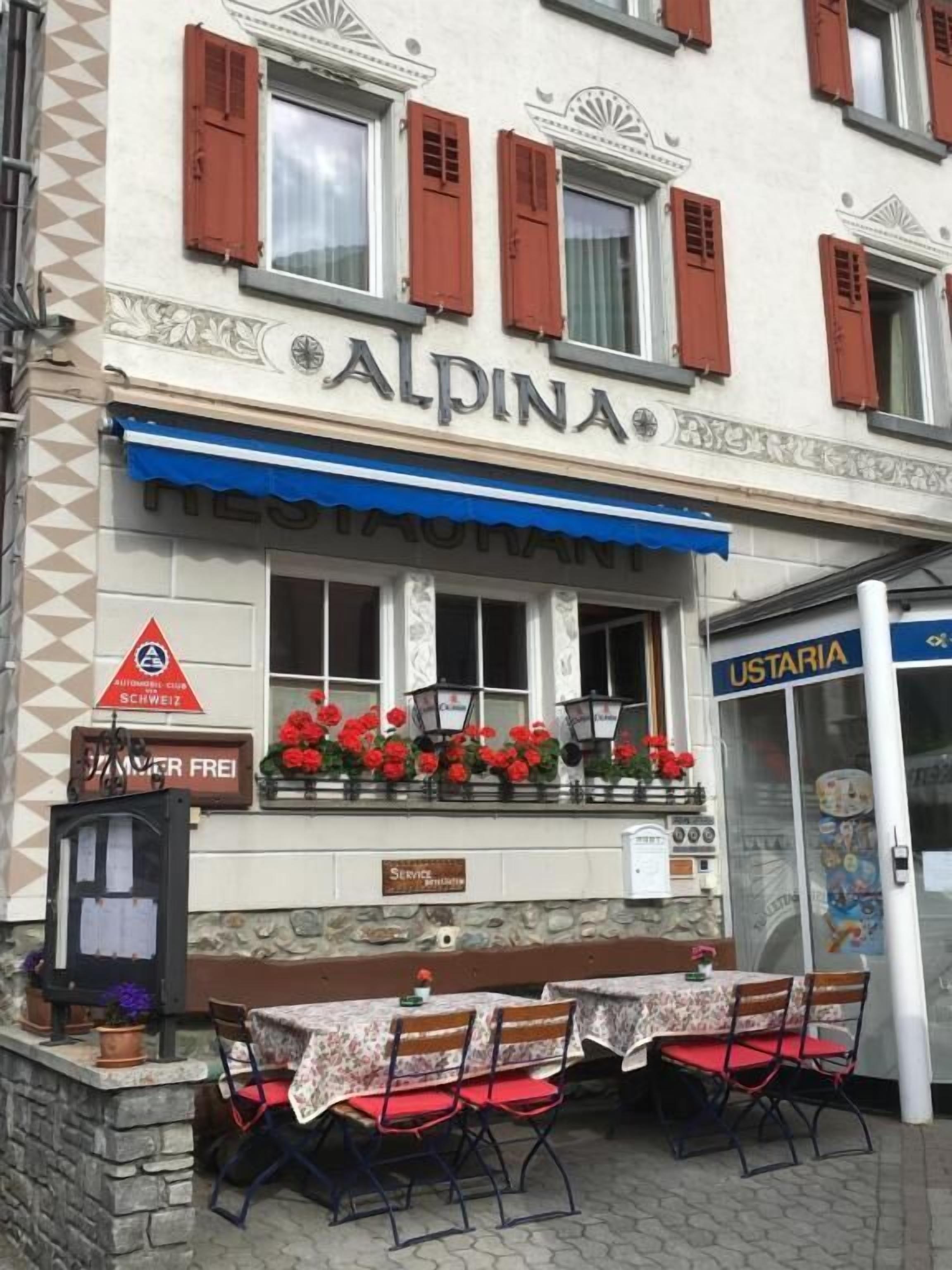 A restaurant named 'ALPINA' with outdoor seating and a sign for 'AUTOMATEN CLUB SCHWEIZ'.