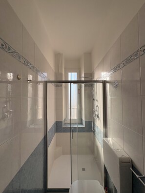 Une salle de bain moderne avec une douche à parois de verre, des murs carrelés et une porte visible donnant sur une autre pièce.