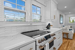 A modern kitchen with a white countertop, a built-in stove, and a view of the outdoors through large windows. - Private Pool, 2 Min Walk to Beach, Perfect for Families and Couples (Isle of Palms)