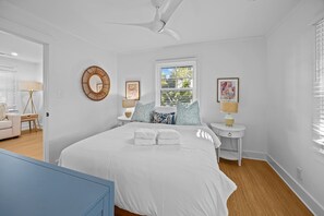 Ein Schlafzimmer mit einem großen Bett, zwei Nachttischen, einem Deckenventilator, einem Fenster mit Jalousien und einem wandmontierten Spiegel.