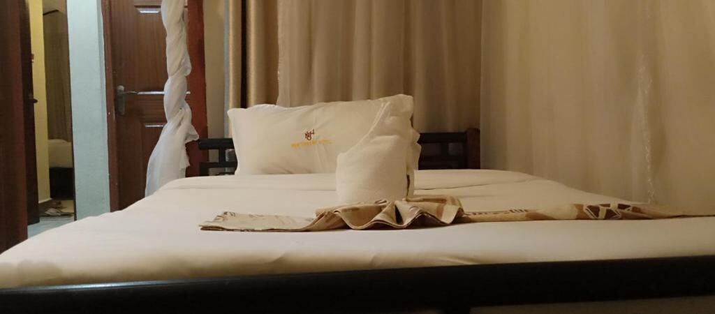 Un lit bien fait, avec une couverture et des oreillers de couleur beige, une tête de lit en bois et un rideau tiré partiellement sur le côté.