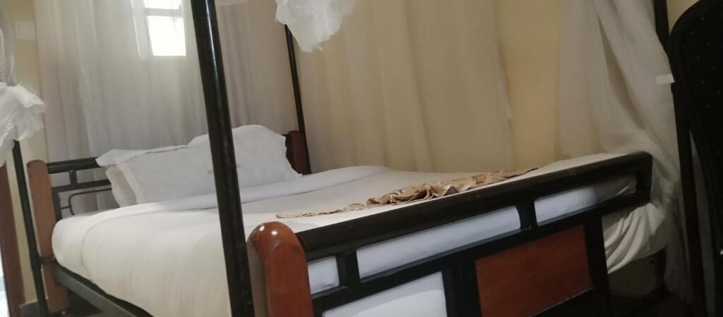Een eenpersoonsbed met houten frame, wit beddengoed en een klamboe.