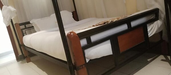 A four-poster bed with white linens, a wooden frame, and a headboard with a decorative panel.