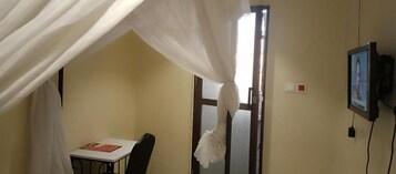 Una habitación con cama, mesa, silla, televisor y puerta.