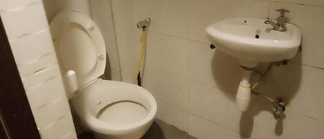 A bathroom with a toilet, a sink, and a yellow cleaning hose.