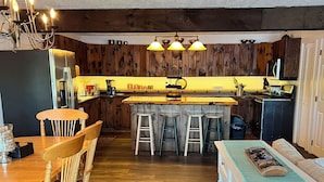 Une cuisine avec des meubles de rangement en bois, un îlot central doté de tabourets, une table à manger avec des chaises et un réfrigérateur.