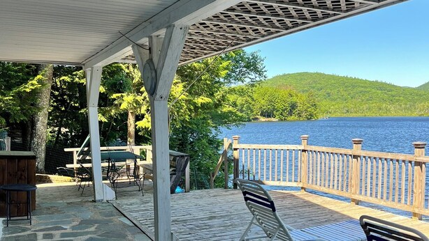 Une terrasse extérieure couverte, dotée d’un sol en pierre, d’une clôture en bois et offrant une vue sur un lac.