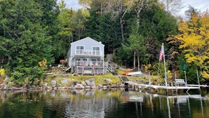Une maison au bord d’un lac, avec un quai, entourée d’arbres et ornée d’un drapeau.