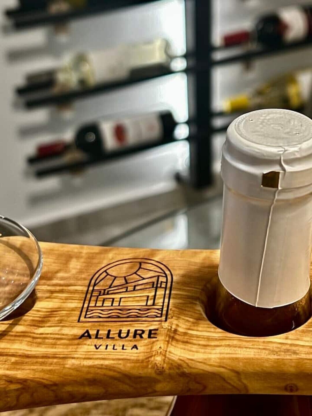 A wooden table with a bottle of wine and a glass. The table has a logo with the text 'ALLURE VILLA'.