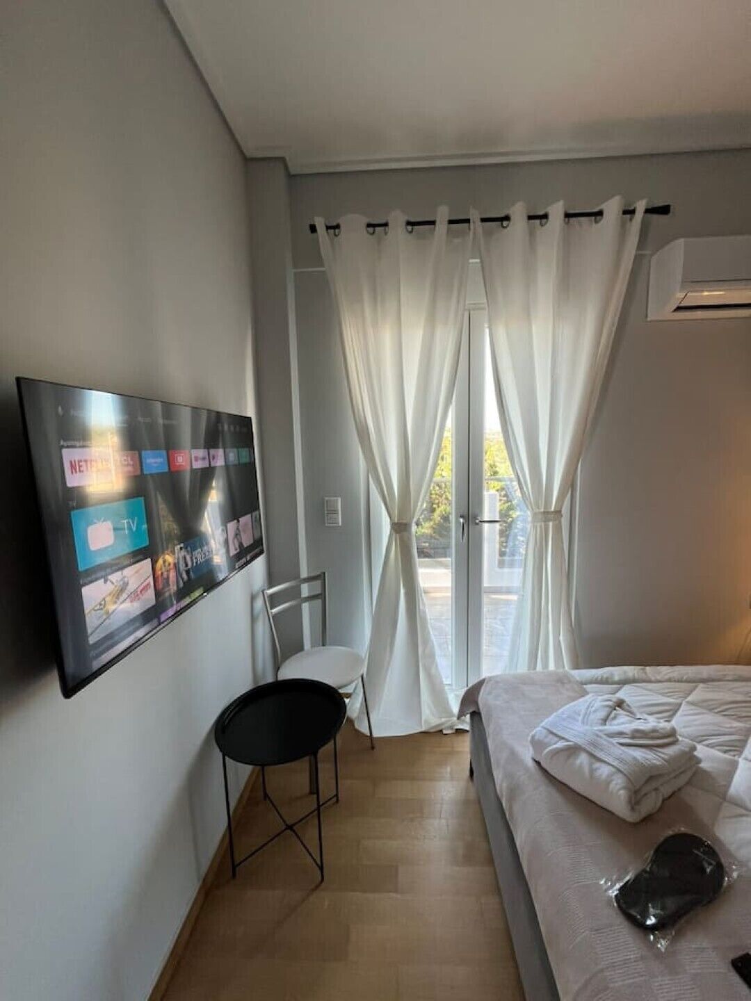 Een hotelkamer met een bed, een tv aan de muur, een stoel en een raam met gordijnen.