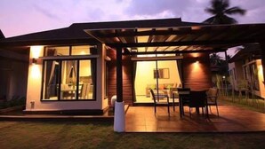 Ein modernes Haus mit überdachter Terrasse, Essbereich und sichtbarem Innenraum mit Sofa und Fernseher.
