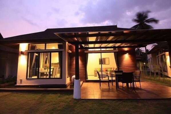 Ein modernes Haus mit überdachter Terrasse, Essbereich und sichtbarem Innenraum mit Sofa und Fernseher.