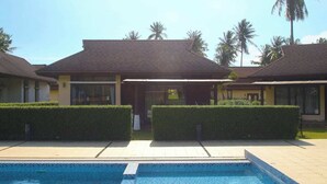 Ein Poolbereich mit klarem, blauem Pool, einem überdachten Sitzbereich und ordentlich gestutzten Hecken.