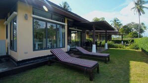 Ein modernes Haus mit großen Fenstern, einer überdachten Terrasse und zwei Lounge-Stühlen.