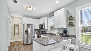 A modern kitchen with white cabinets, stainless steel appliances, a granite countertop, and a view of the outdoors. - 30A - Hidden Lakes Condo Rentals (Santa Rosa Beach)