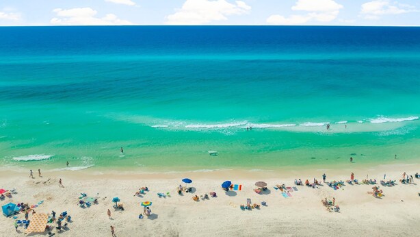 A beach with clear turquoise water, a sandy shore, and people sunbathing. - 30A - Hidden Lakes Condo Rentals (Santa Rosa Beach)