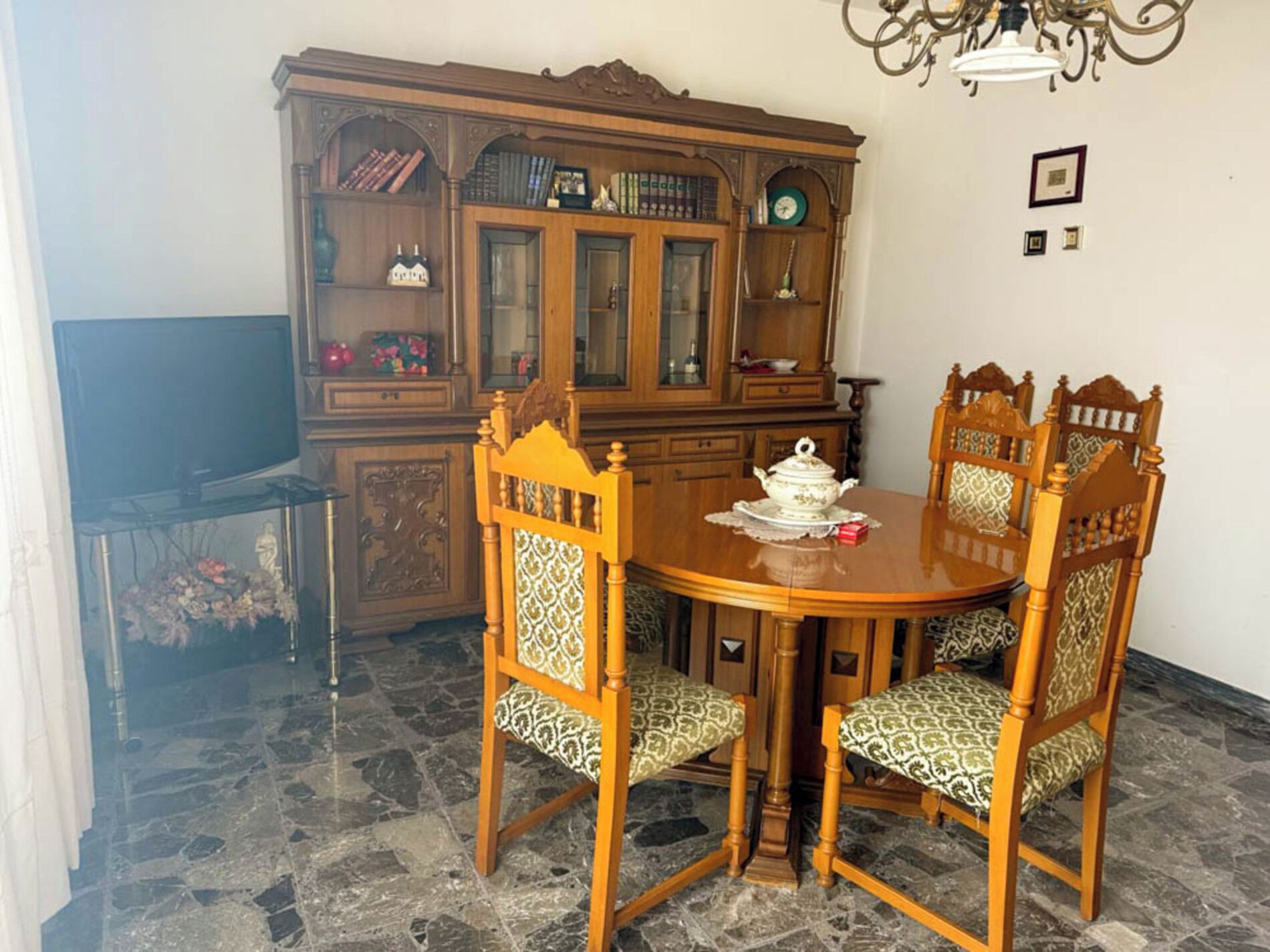 Un coin repas avec une table et des chaises en bois, un buffet aux portes vitrées et un lustre.