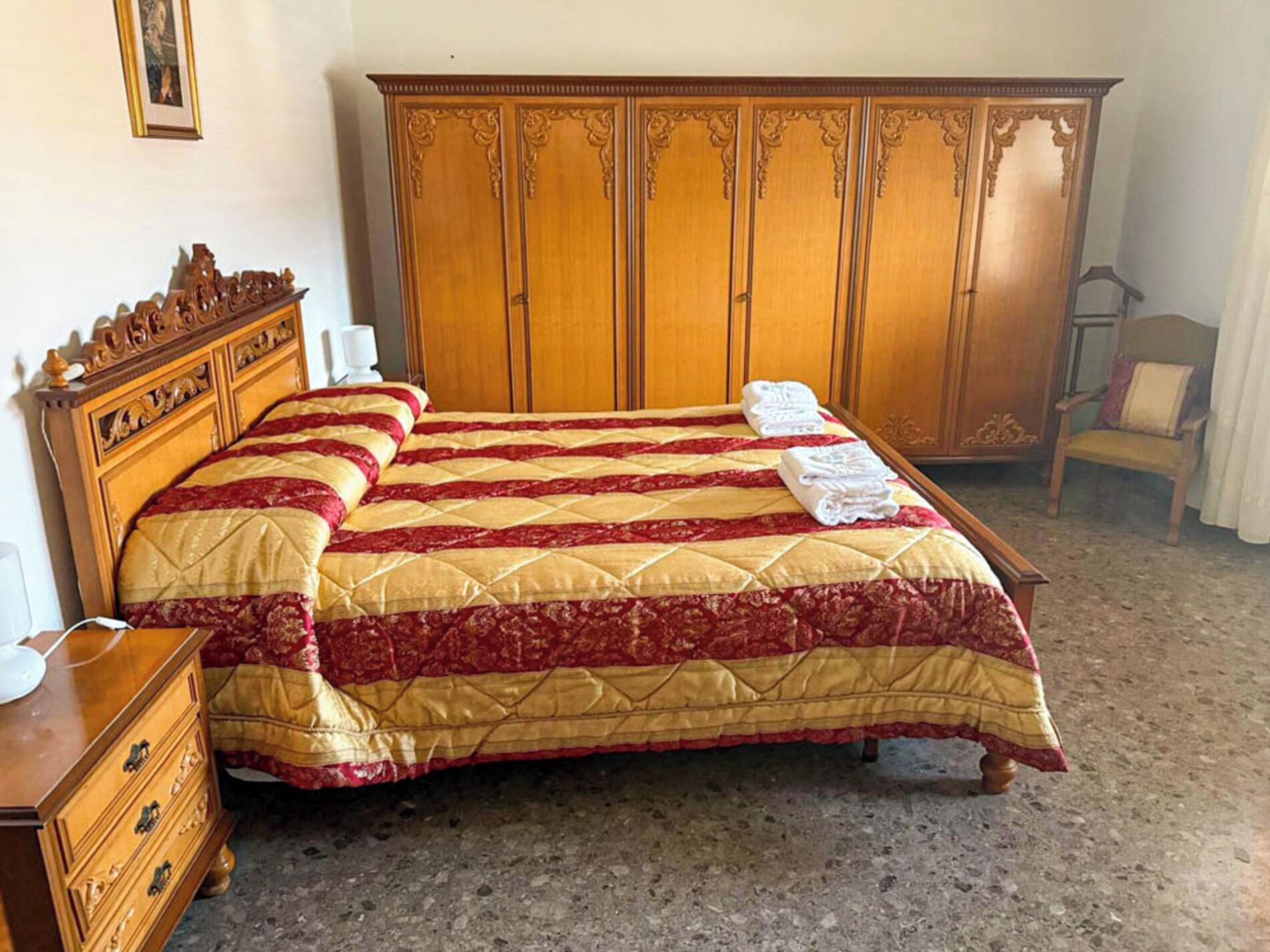 A bedroom with a large bed, wooden wardrobe, and a nightstand.