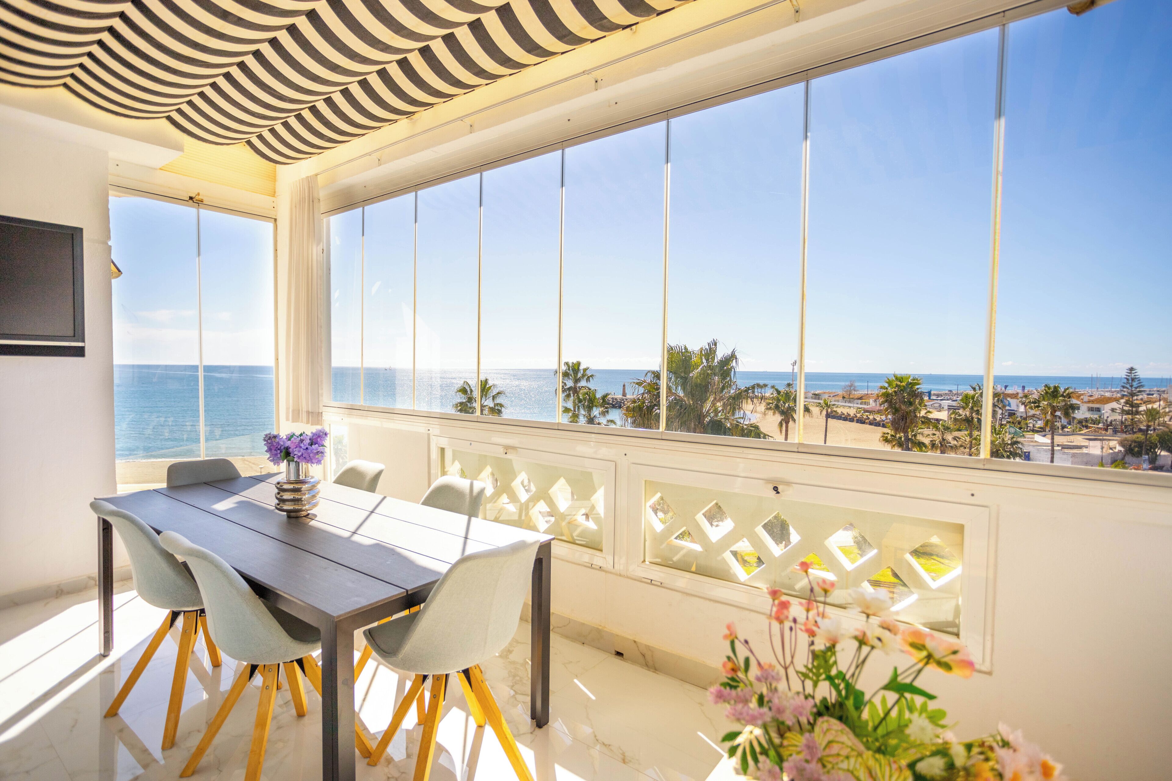 Un comedor con vista al mar, una mesa con sillas y un jarrón con flores.